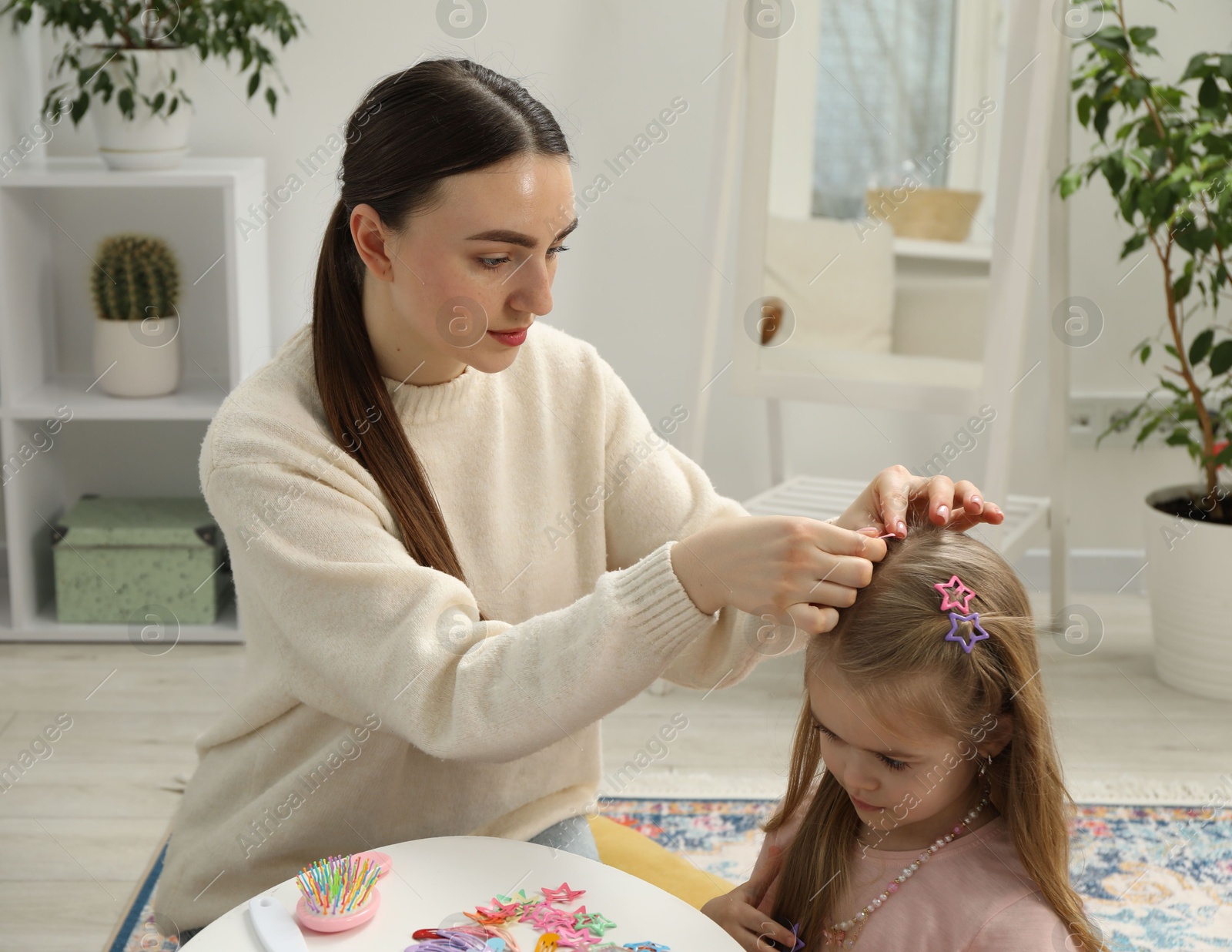 Photo of Mom putting cute accessories onto her daughter's hair at home