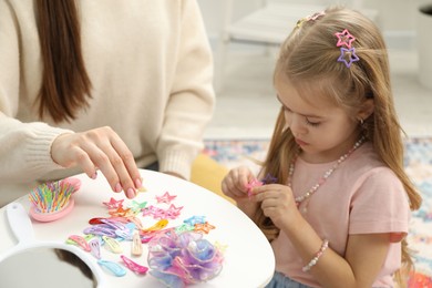 Photo of Mom putting cute accessories onto her daughter's hair at home, closeup