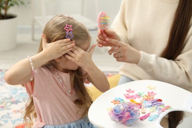 Photo of Mom putting cute accessories onto her daughter's hair at home, closeup