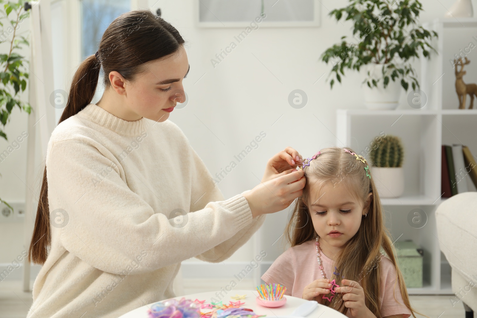 Photo of Mom putting cute accessories onto her daughter's hair at home