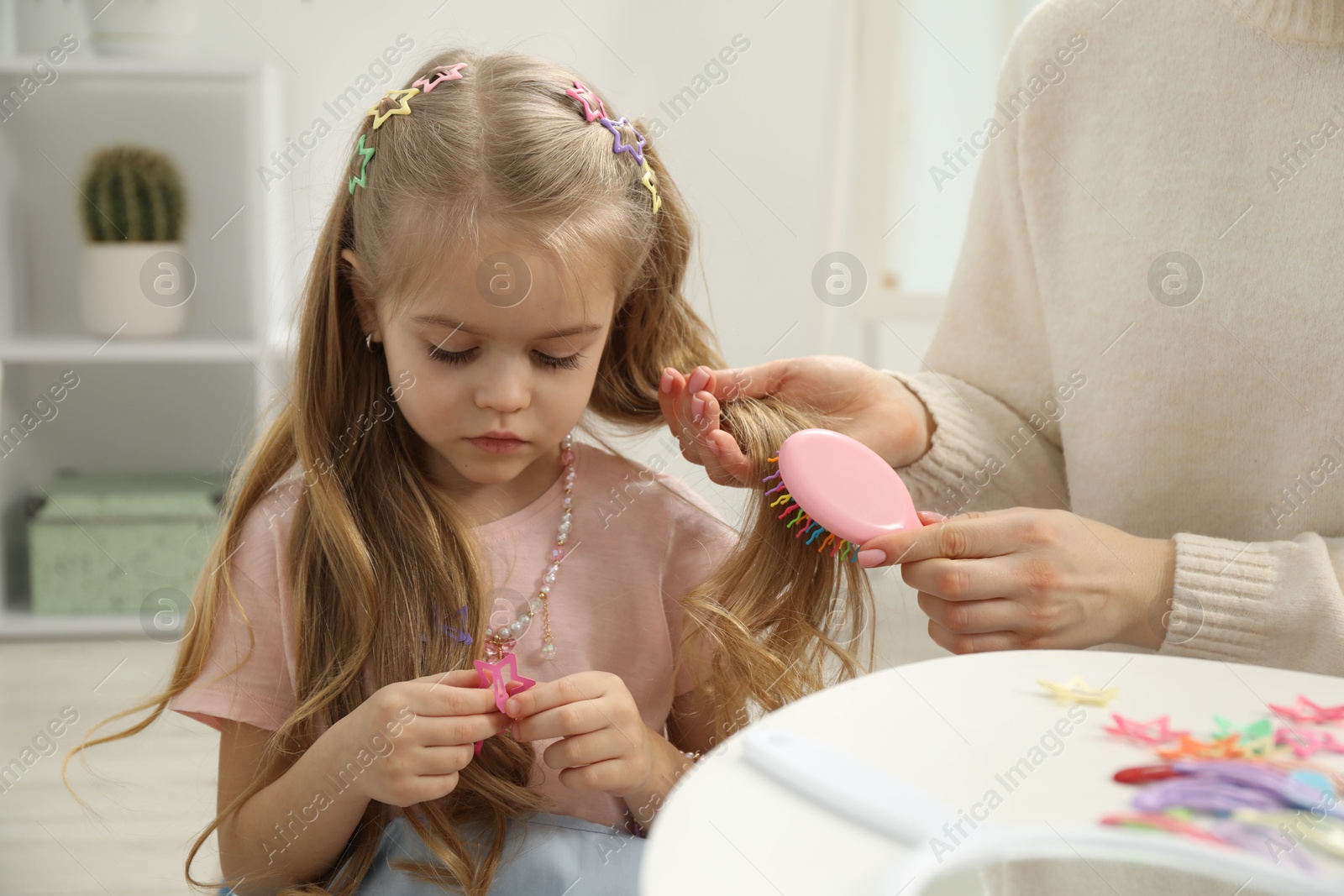 Photo of Mother brushing her little daughter's hair at home, closeup