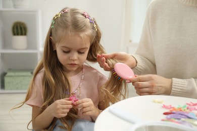 Photo of Mother brushing her little daughter's hair at home, closeup