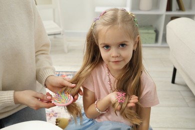 Photo of Mother brushing her little daughter's hair at home, closeup