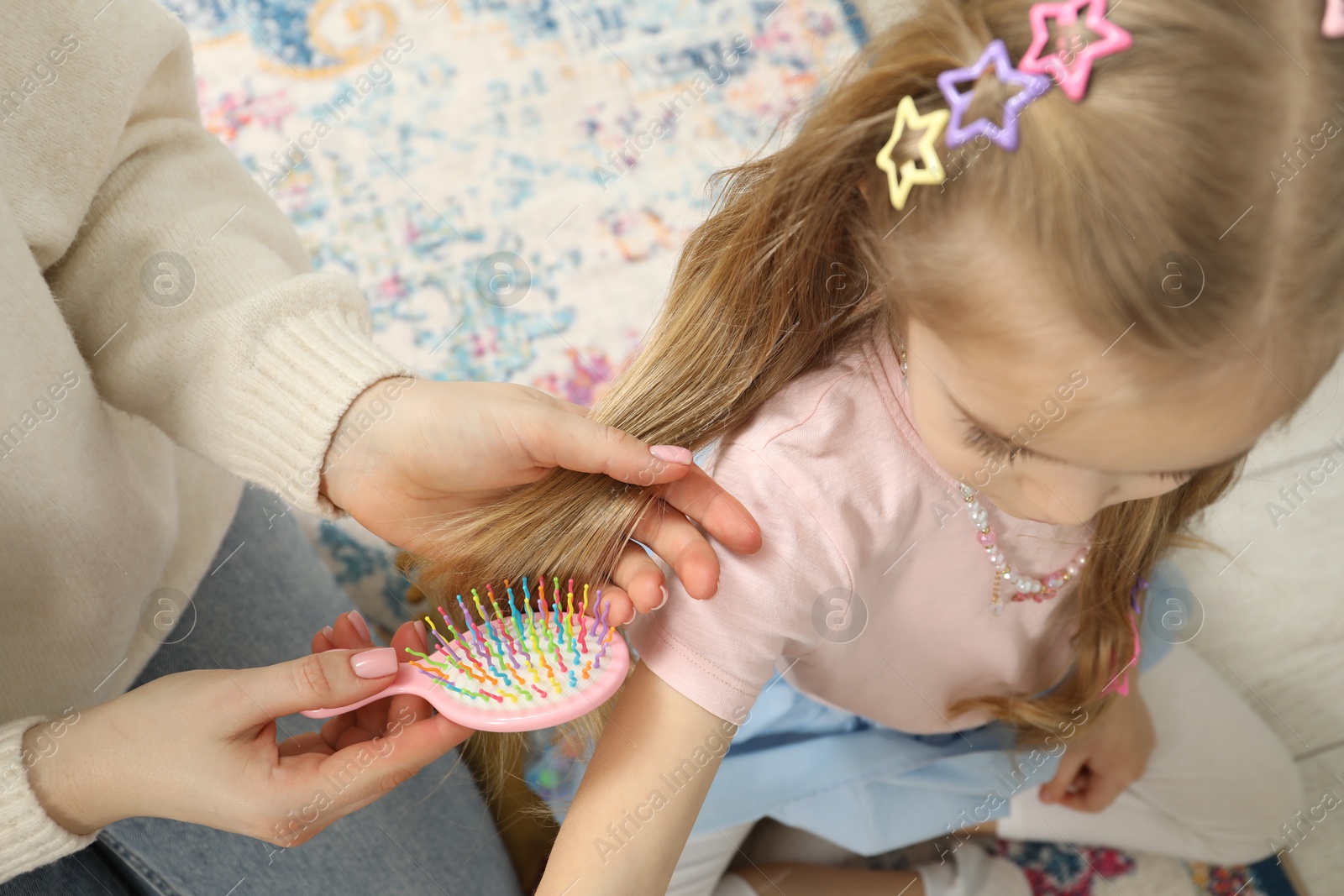 Photo of Mother brushing her little daughter's hair at home, closeup