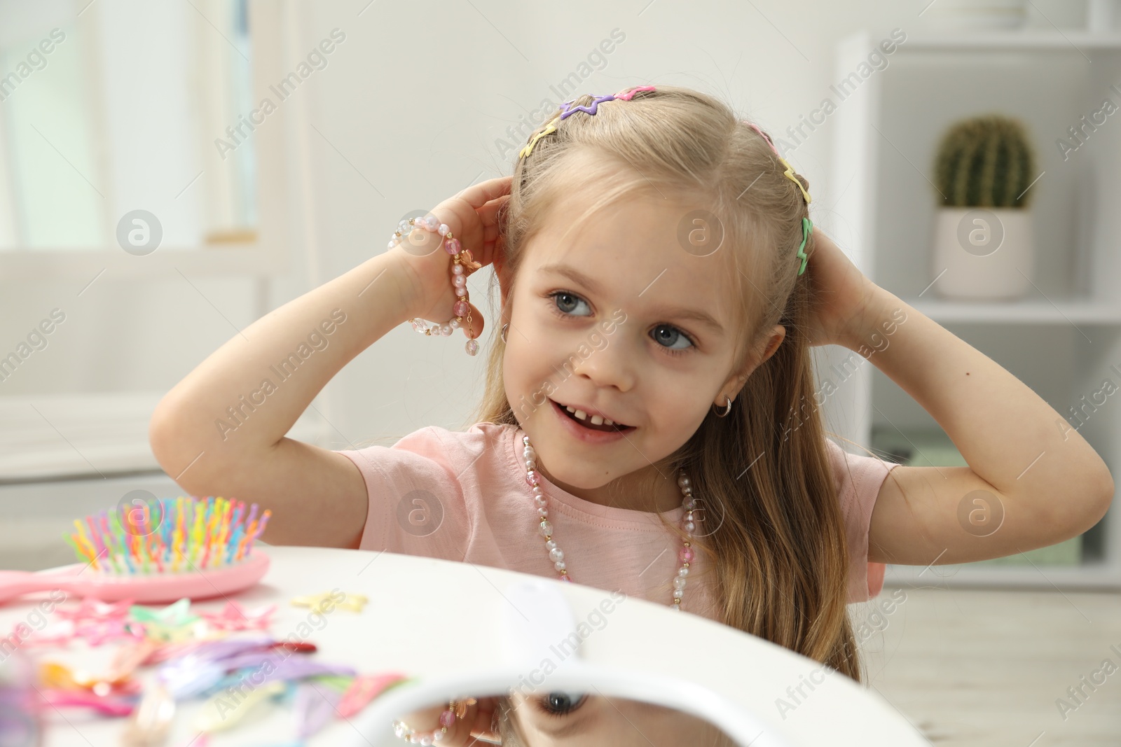 Photo of Little girl with many cute hair accessories at table indoors