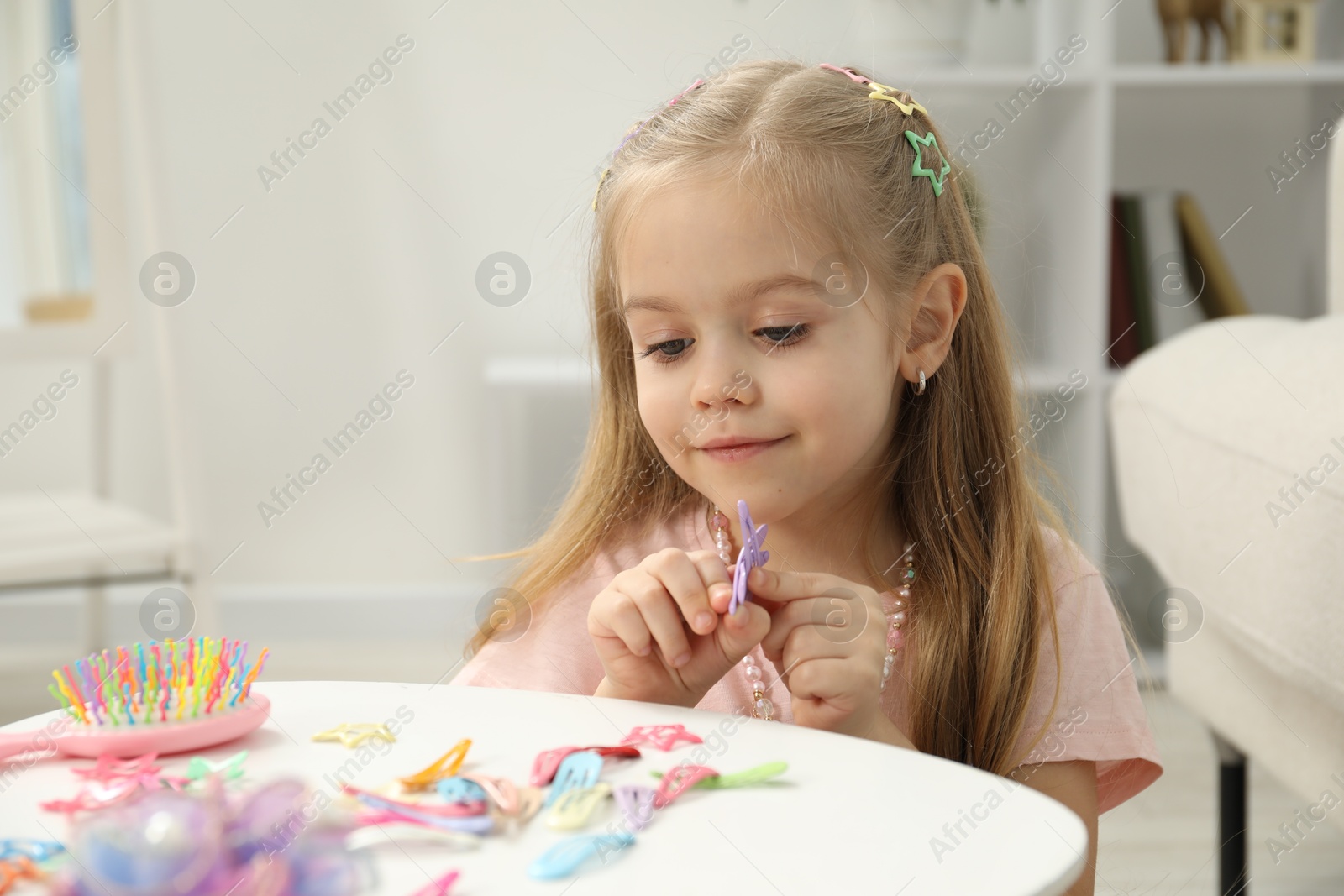 Photo of Little girl with many cute hair accessories at table indoors. Space for text