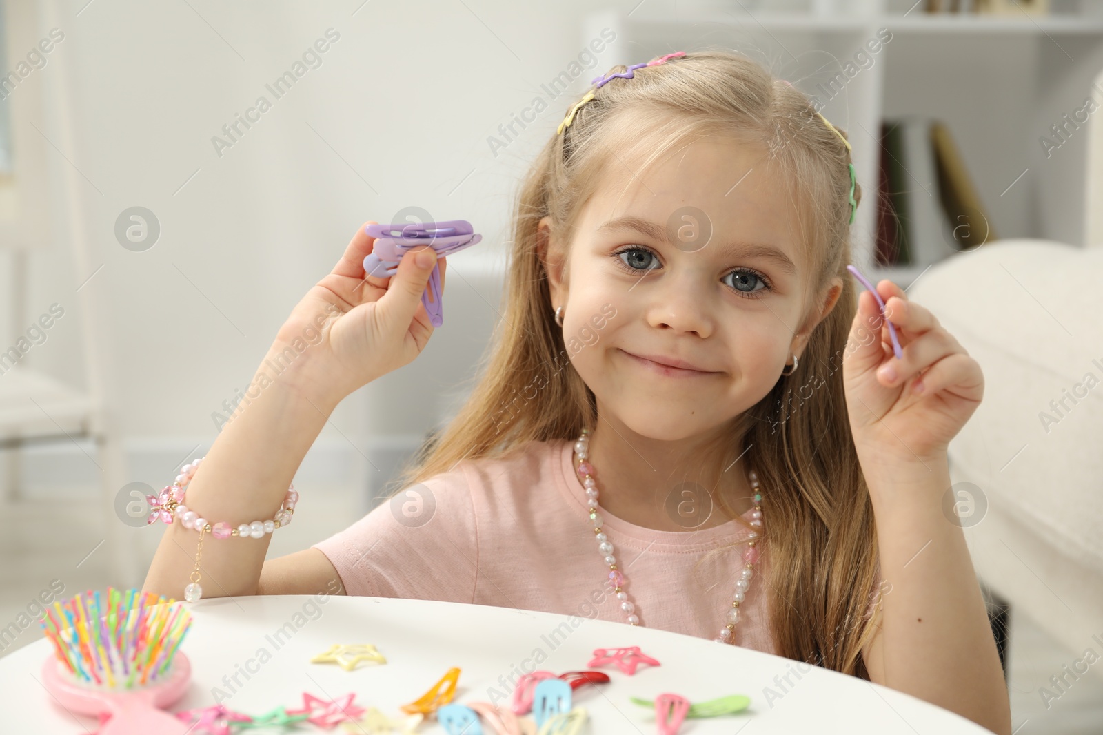 Photo of Little girl with many cute hair accessories at table indoors