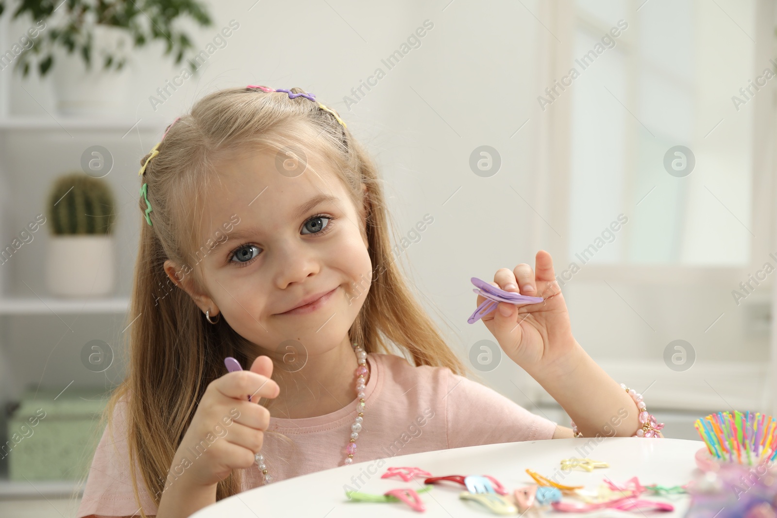 Photo of Little girl with many cute hair accessories at table indoors. Space for text