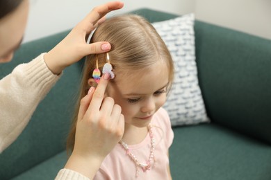 Photo of Mom putting cute accessories onto her daughter's hair at home, closeup