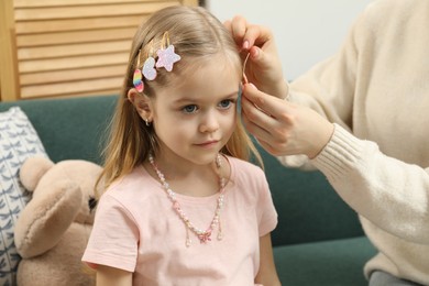 Photo of Mom putting cute accessories onto her daughter's hair at home, closeup