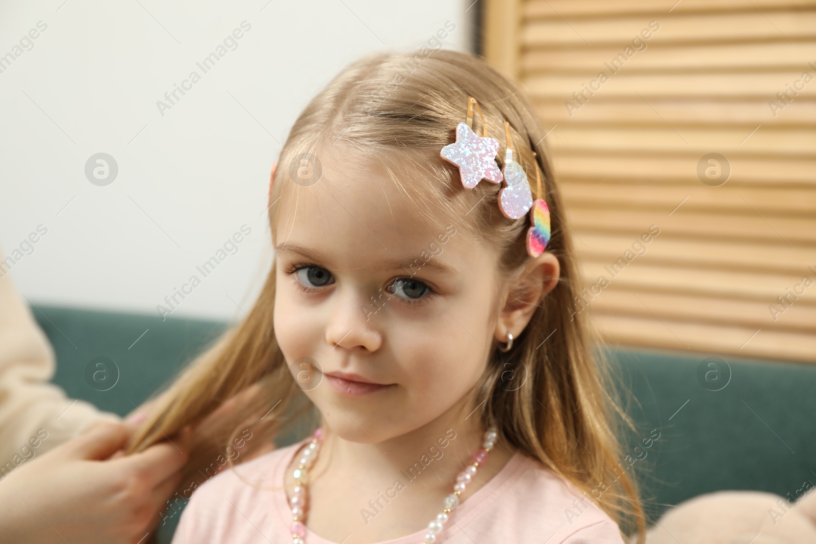 Photo of Mom putting cute accessories onto her daughter's hair at home, closeup