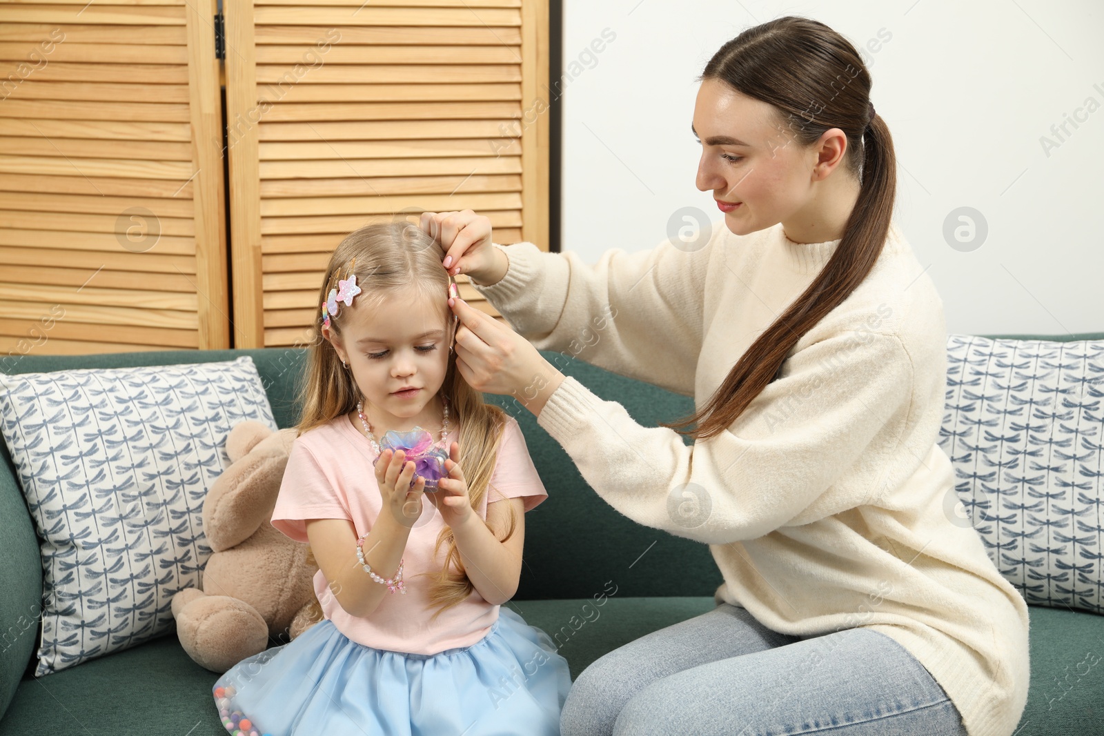 Photo of Mom putting cute accessories onto her daughter's hair at home