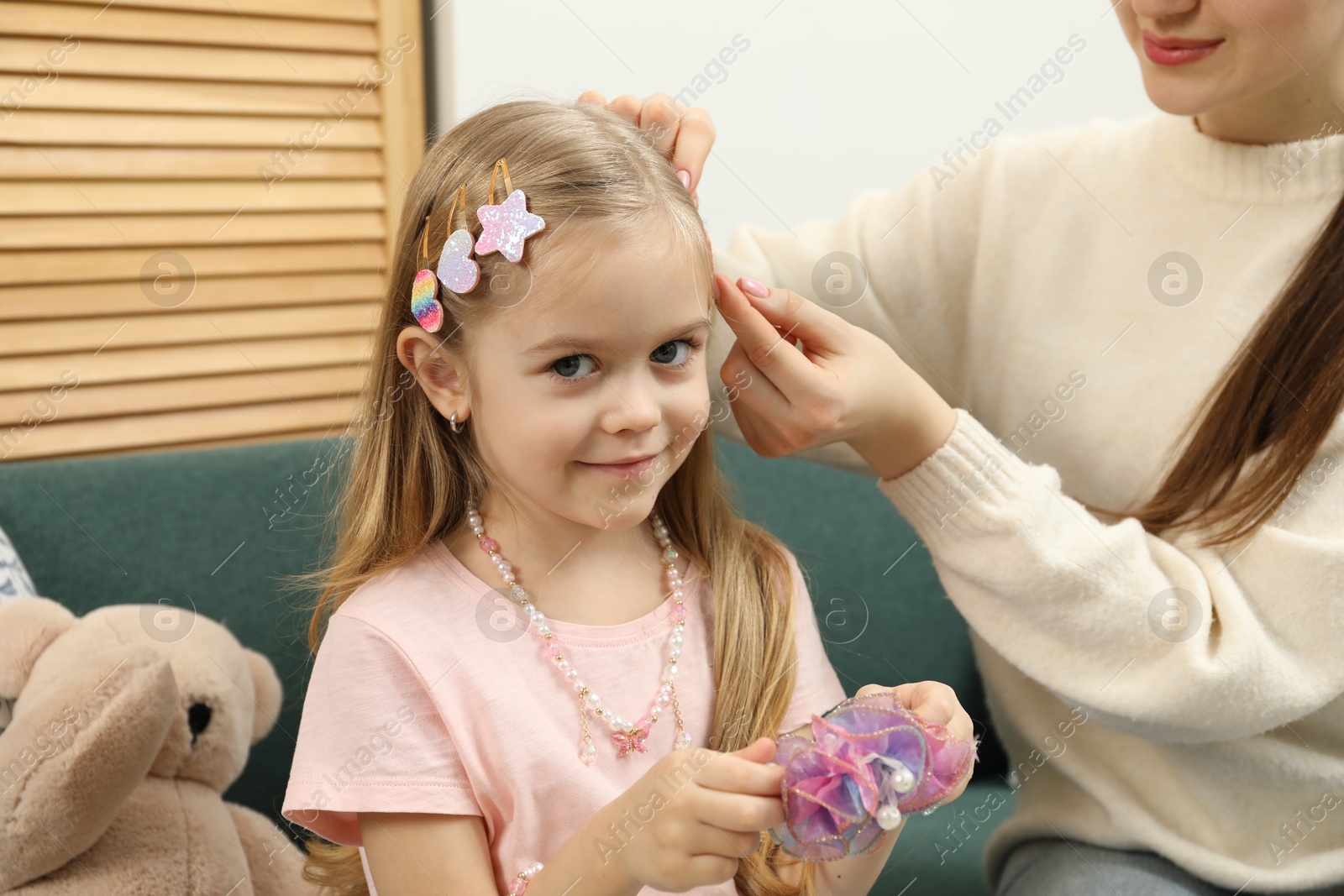 Photo of Mom putting cute accessories onto her daughter's hair at home, closeup