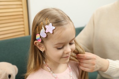 Photo of Mom putting cute accessories onto her daughter's hair at home, closeup