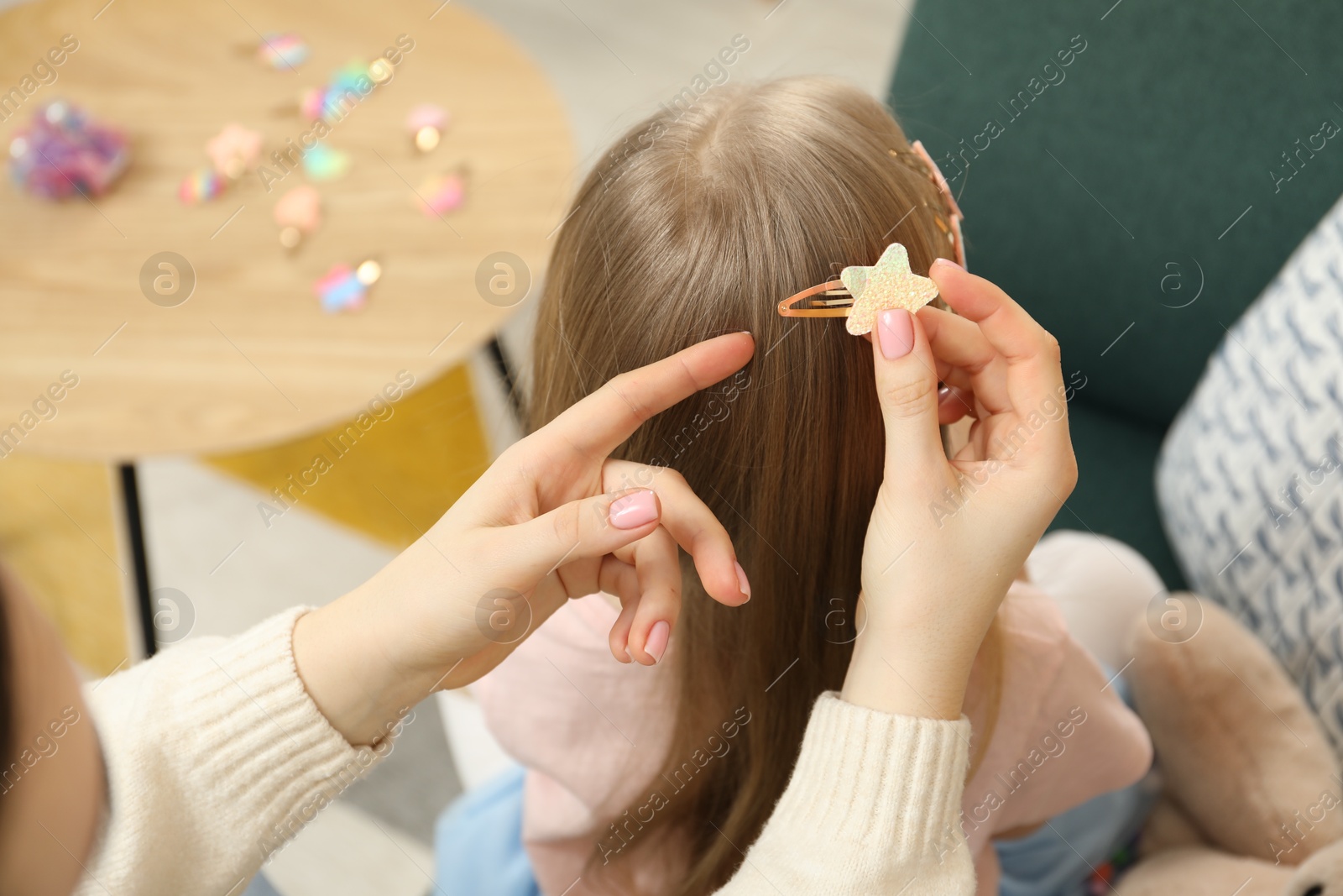 Photo of Mom putting cute accessories onto her daughter's hair at home, closeup