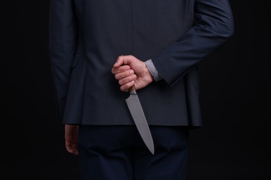 Photo of Businessman holding knife behind his back on black background, closeup