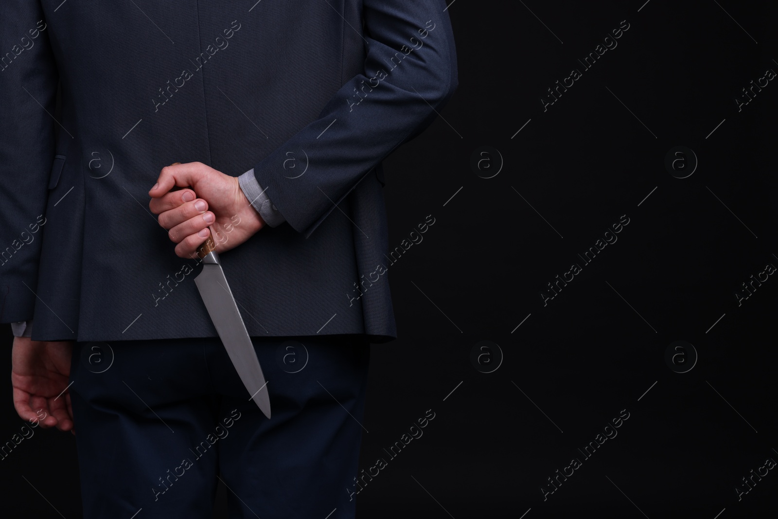 Photo of Businessman holding knife behind his back on black background, closeup. Space for text