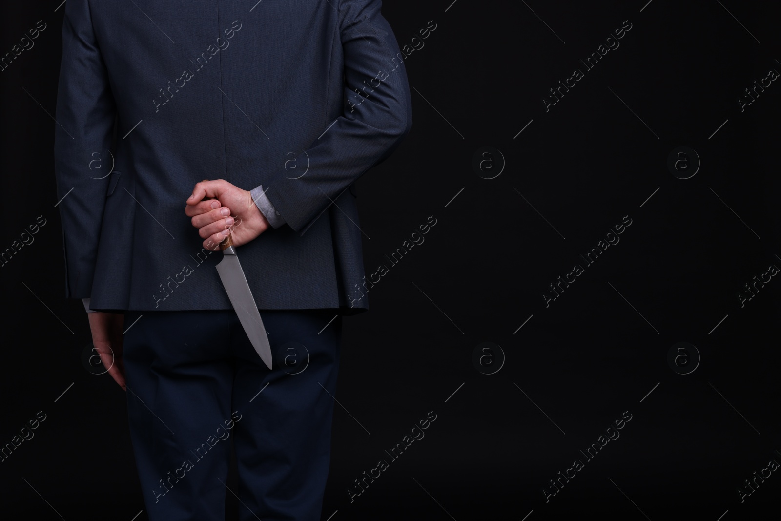 Photo of Businessman holding knife behind his back on black background, closeup. Space for text