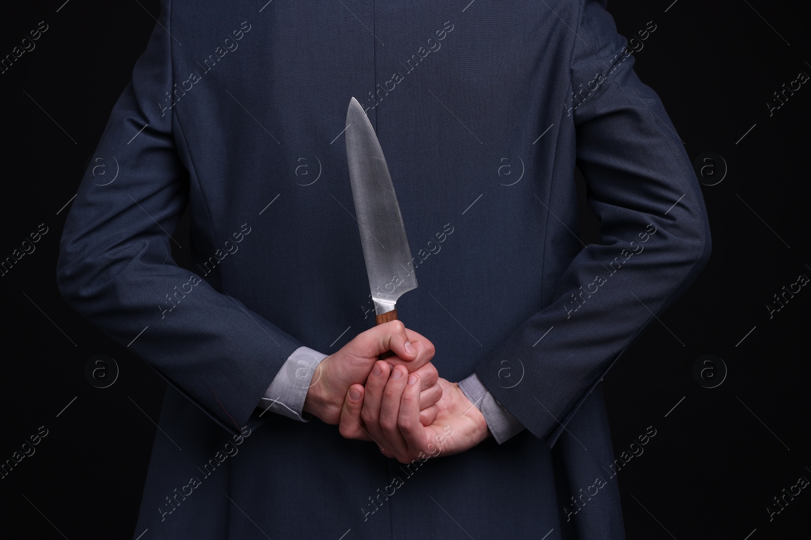 Photo of Businessman holding knife behind his back on black background, closeup