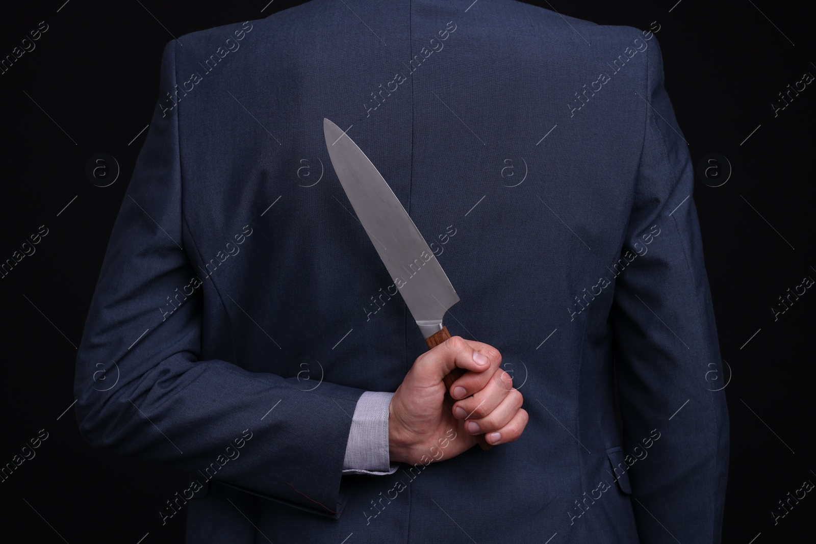 Photo of Businessman holding knife behind his back on black background, closeup