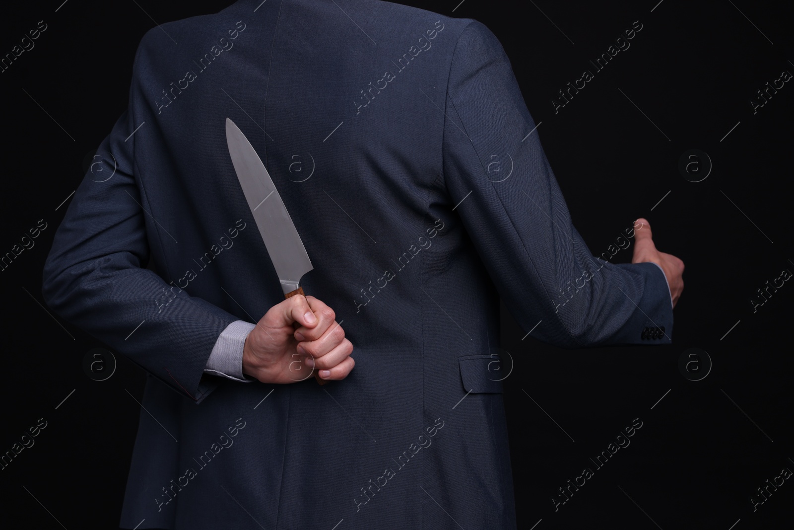 Photo of Businessman holding knife behind his back and offering handshake on black background, closeup