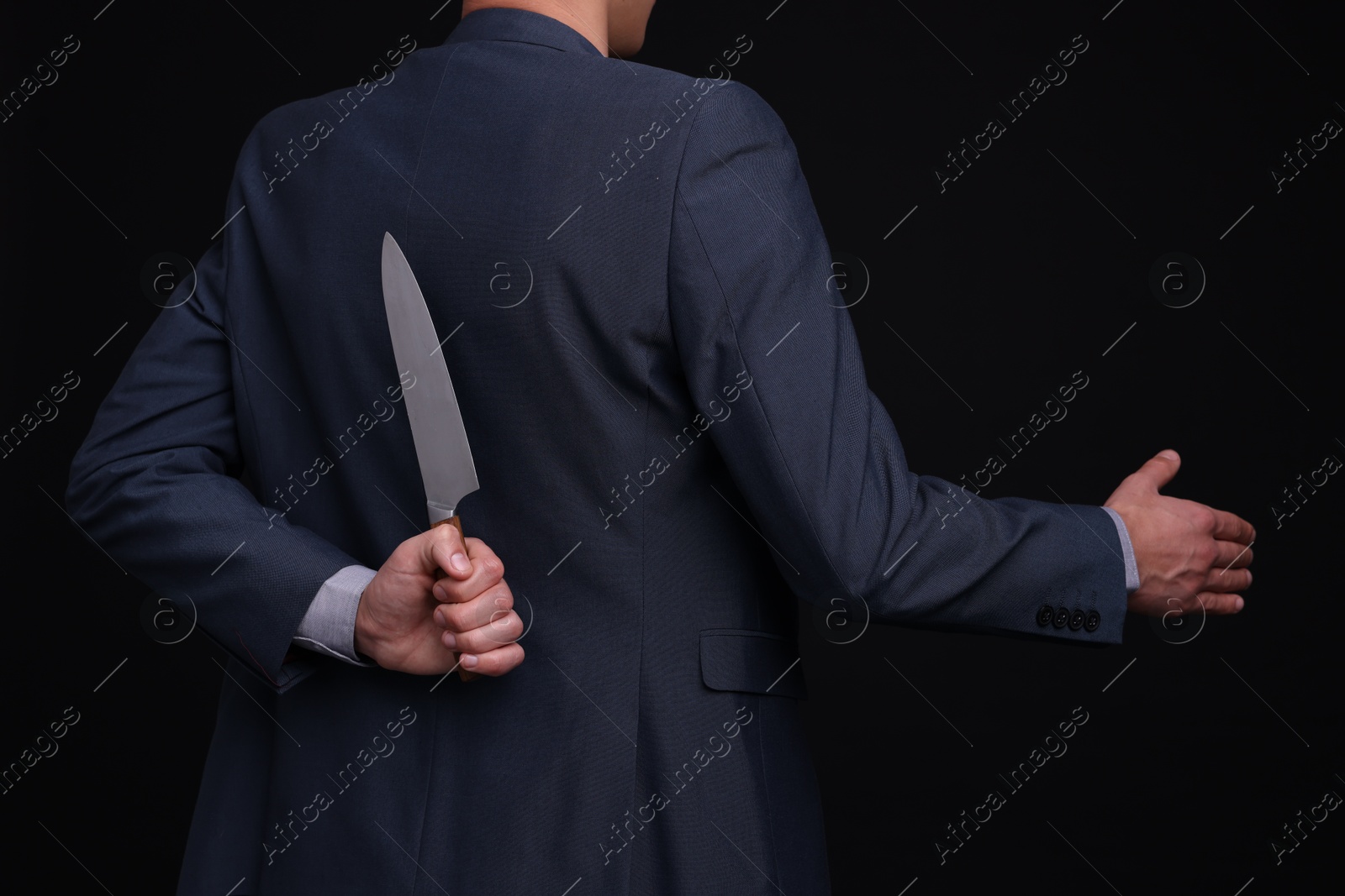 Photo of Businessman holding knife behind his back and offering handshake on black background, closeup