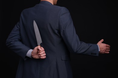 Photo of Businessman holding knife behind his back and offering handshake on black background, closeup