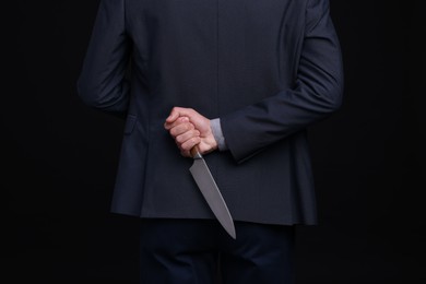 Photo of Businessman holding knife behind his back on black background, closeup