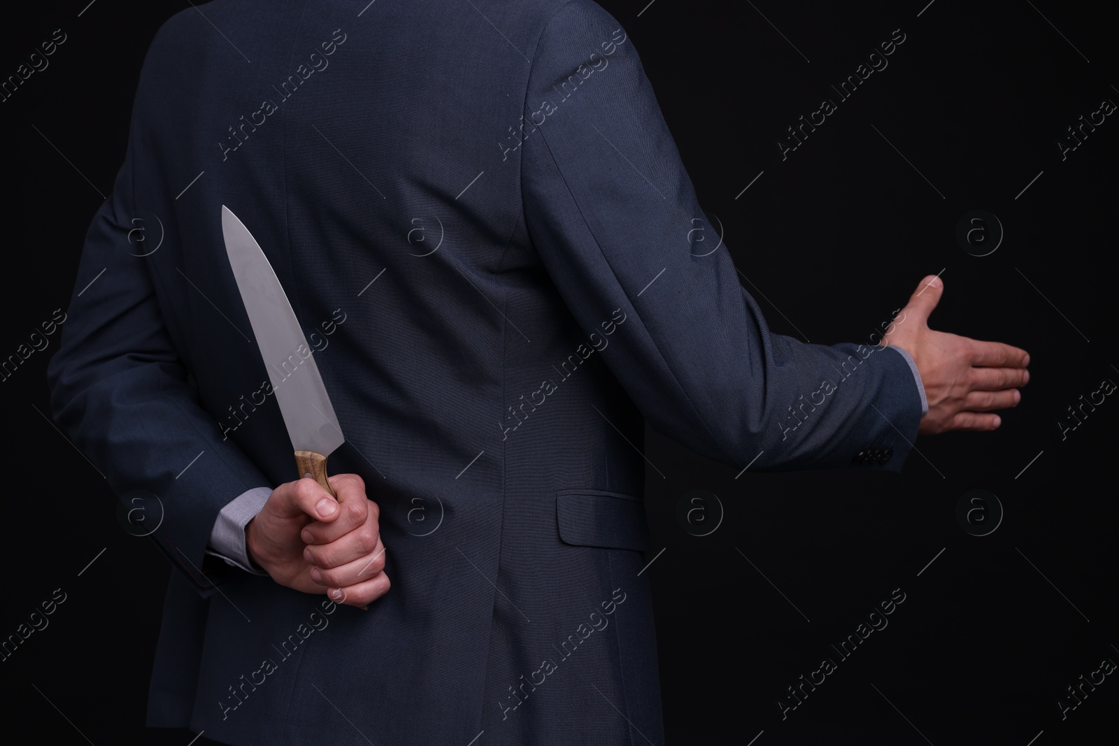 Photo of Businessman holding knife behind his back and offering handshake on black background, closeup