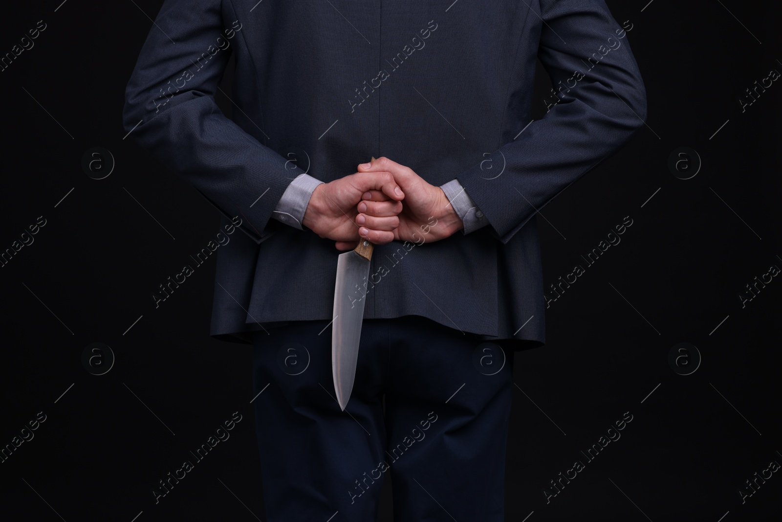 Photo of Businessman holding knife behind his back on black background, closeup