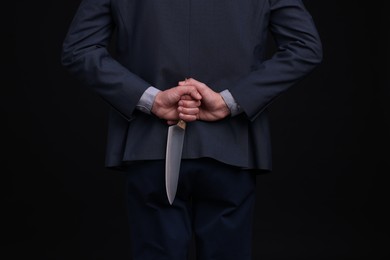 Photo of Businessman holding knife behind his back on black background, closeup