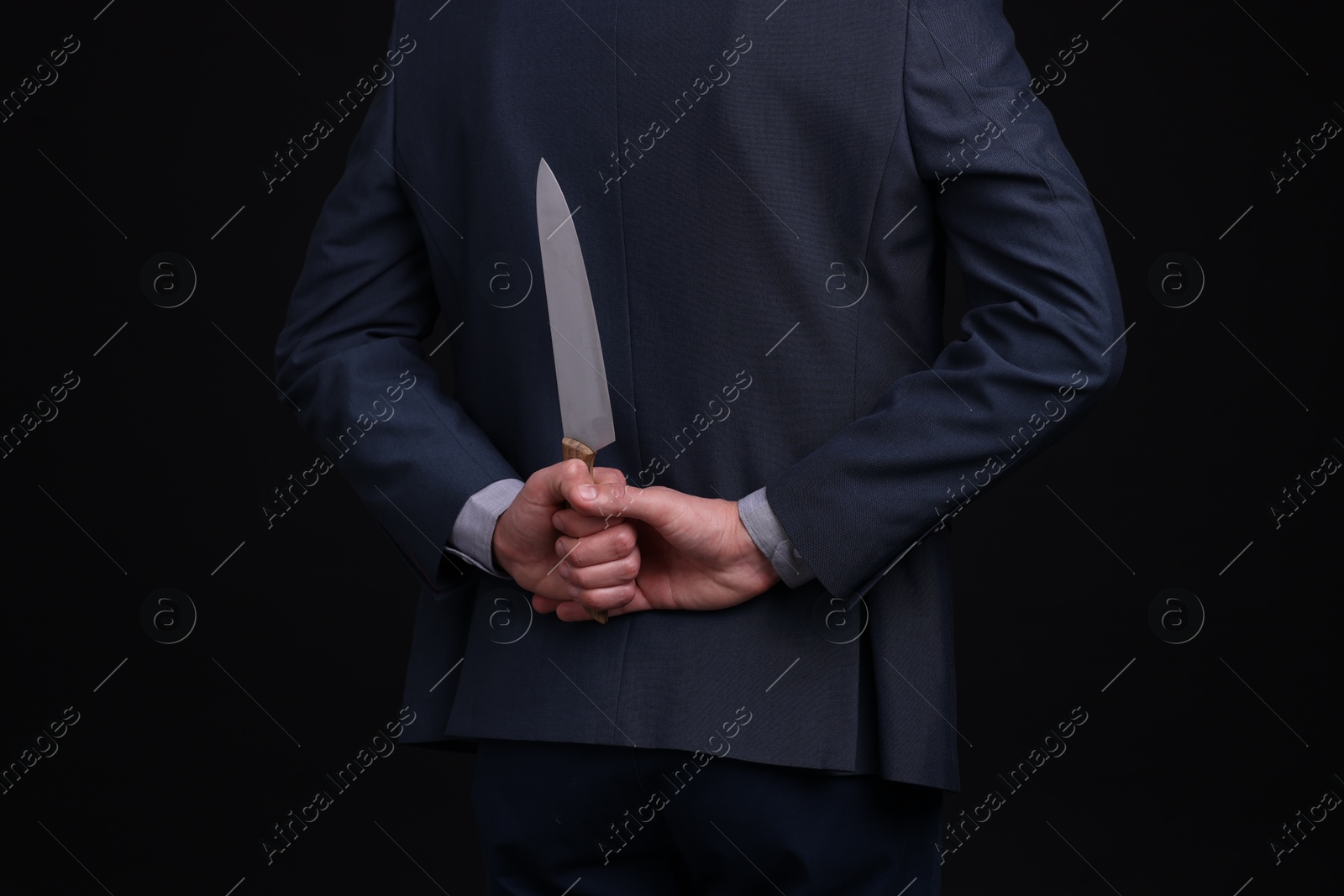 Photo of Businessman holding knife behind his back on black background, closeup