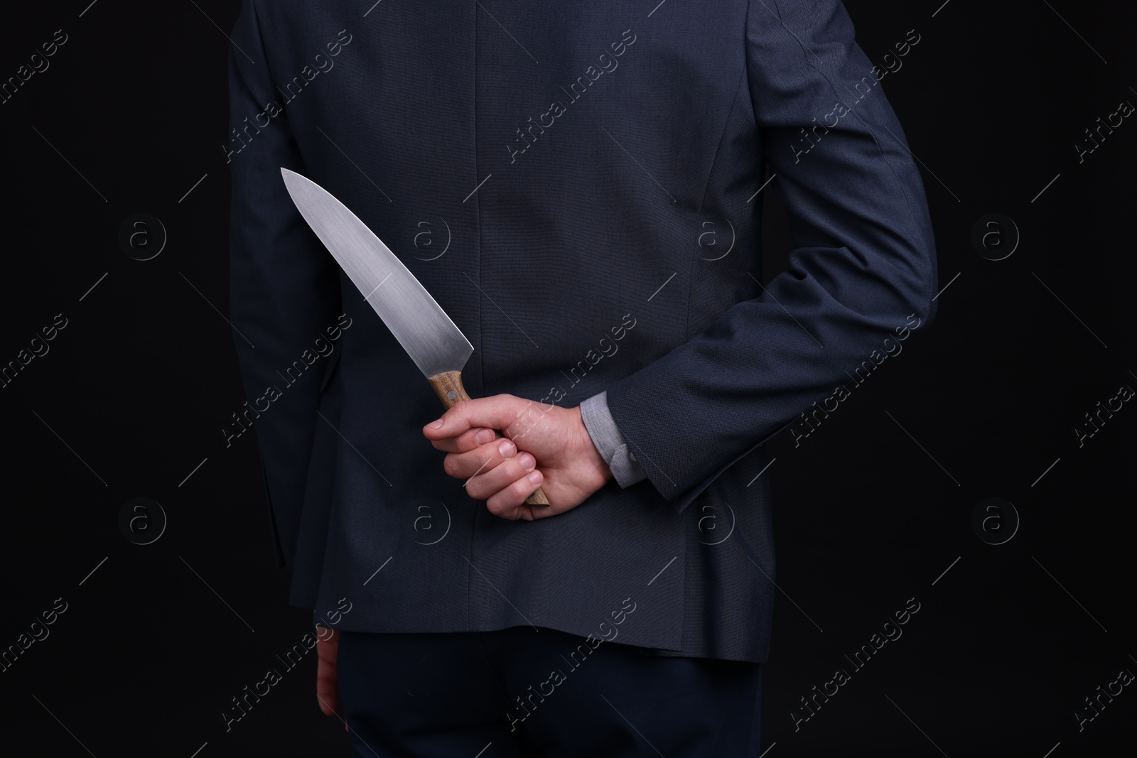 Photo of Businessman holding knife behind his back on black background, closeup