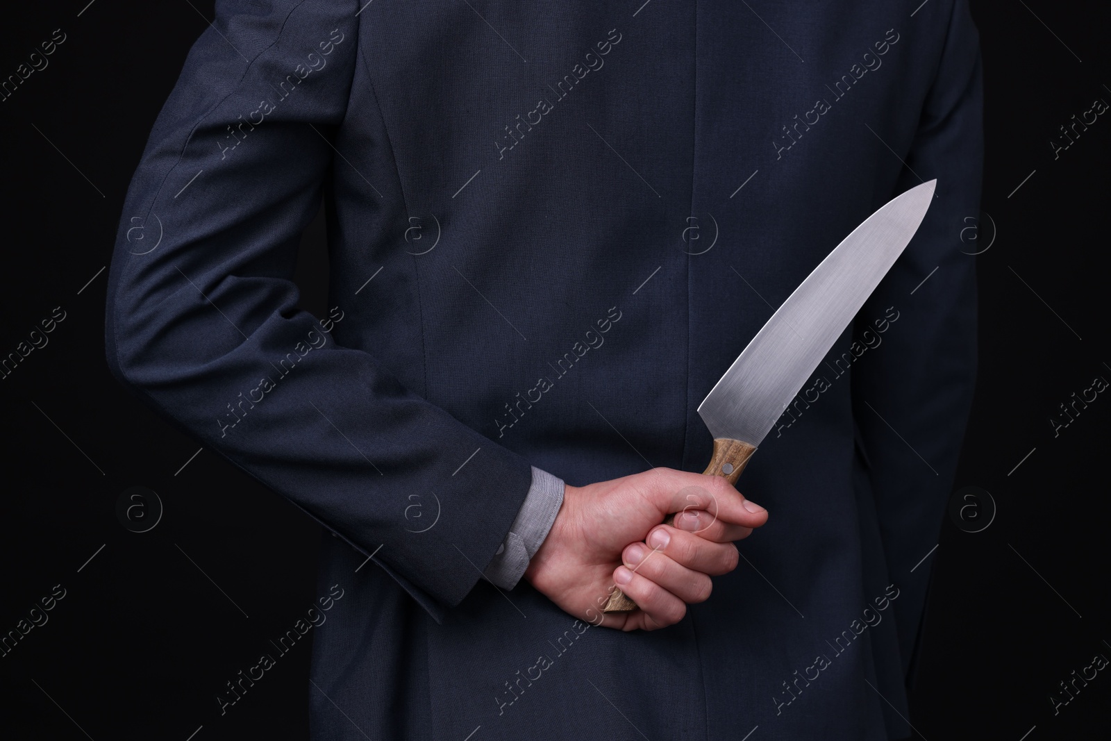 Photo of Businessman holding knife behind his back on black background, closeup