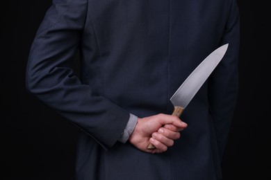 Photo of Businessman holding knife behind his back on black background, closeup