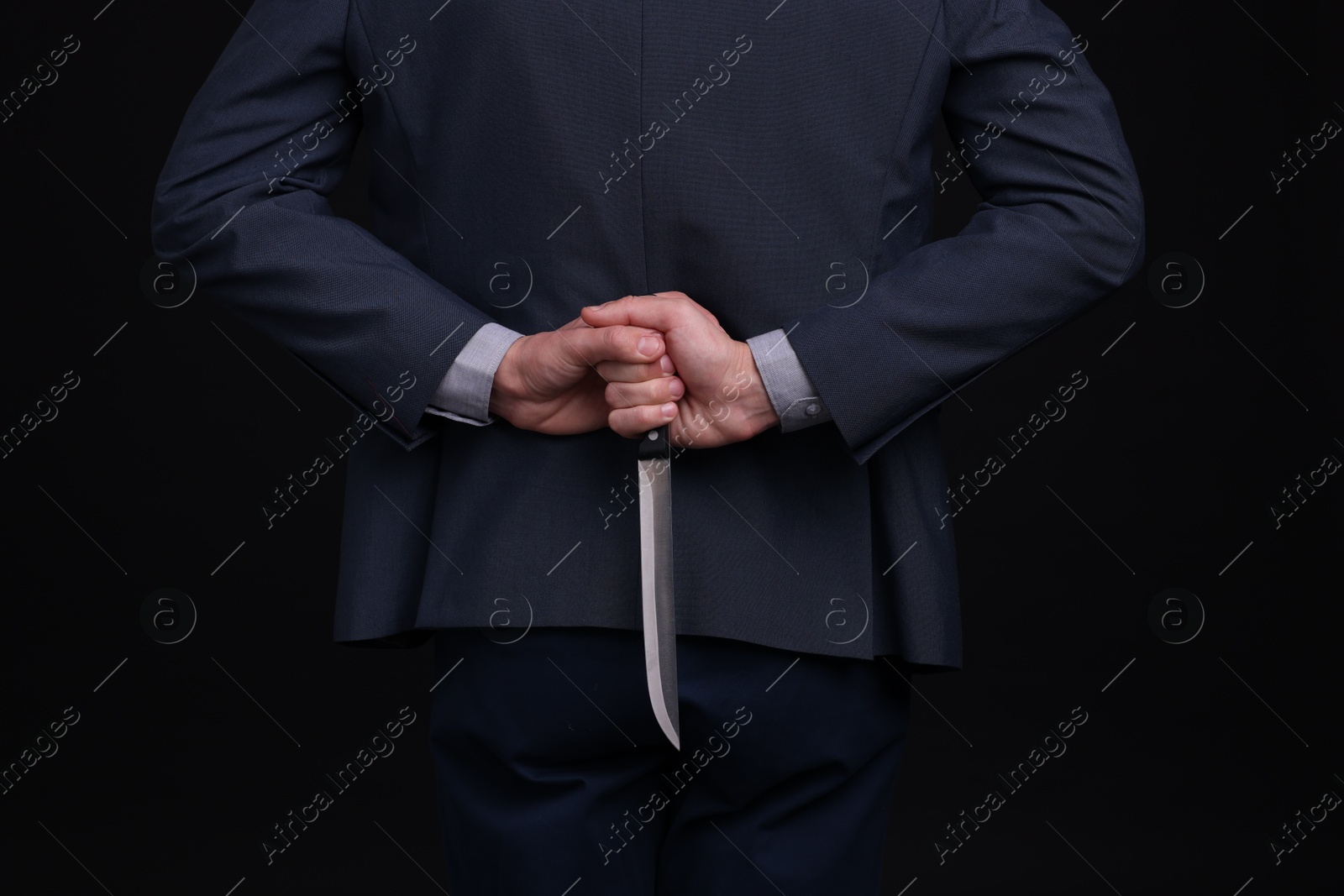 Photo of Businessman holding knife behind his back on black background, closeup