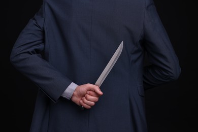 Photo of Businessman holding knife behind his back on black background, closeup