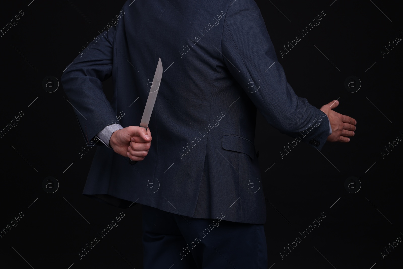 Photo of Businessman holding knife behind his back and offering handshake on black background, closeup