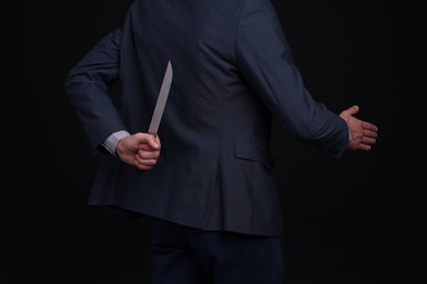 Photo of Businessman holding knife behind his back and offering handshake on black background, closeup