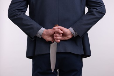 Photo of Businessman holding knife behind his back on white background, closeup