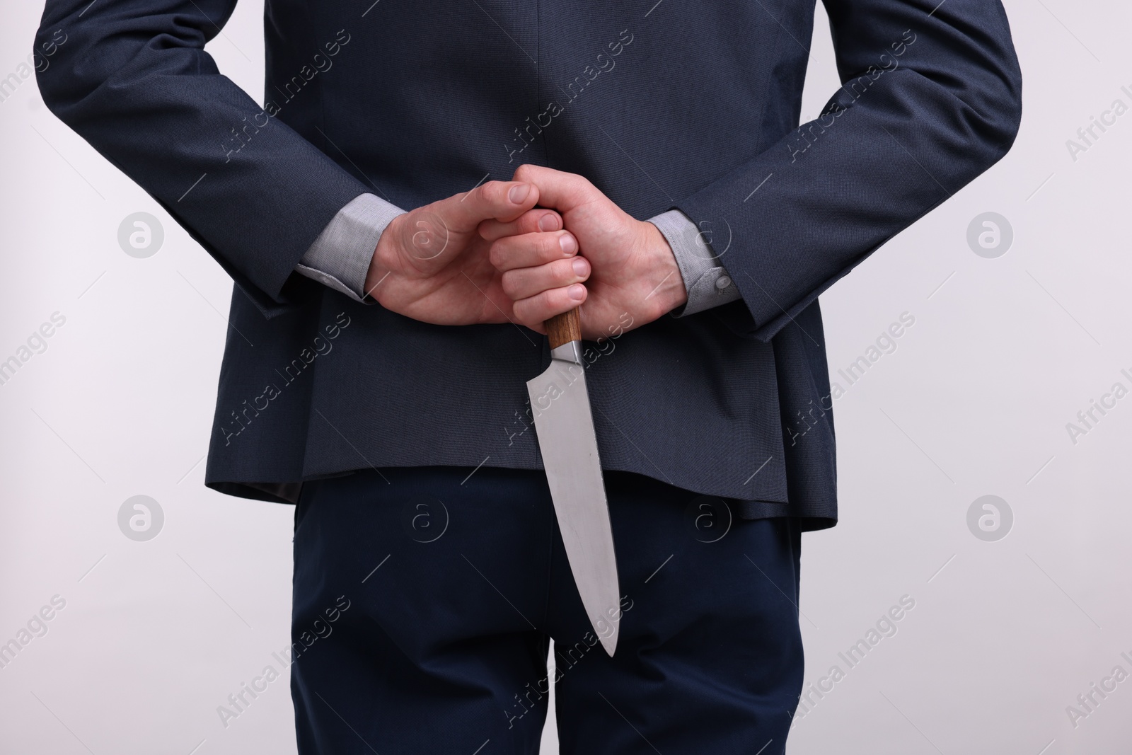 Photo of Businessman holding knife behind his back on white background, closeup