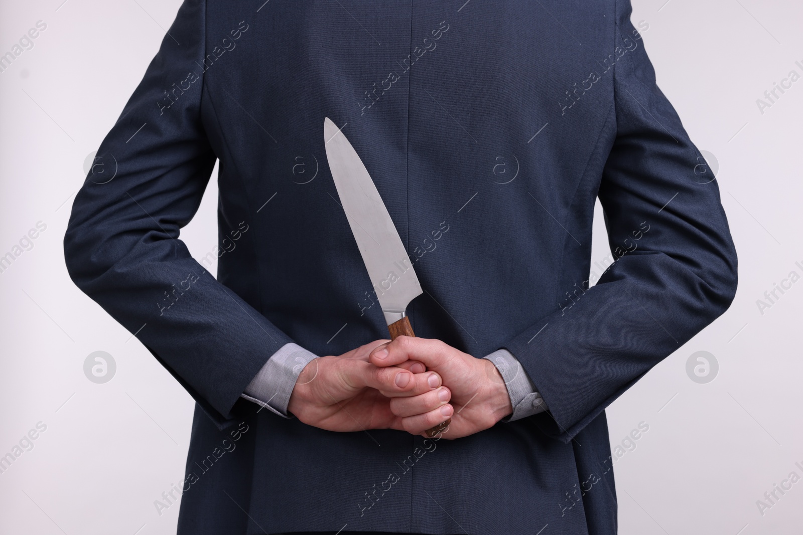 Photo of Businessman holding knife behind his back on white background, closeup