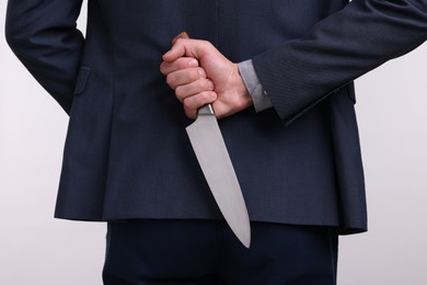 Photo of Businessman holding knife behind his back on white background, closeup