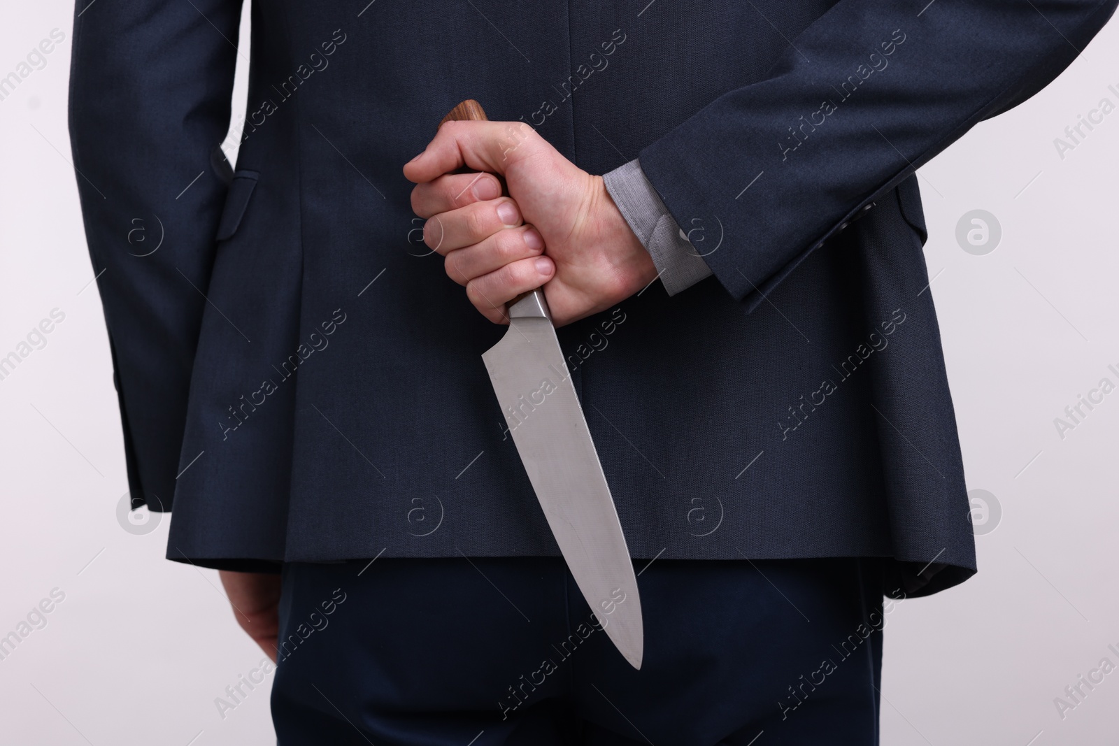 Photo of Businessman holding knife behind his back on white background, closeup