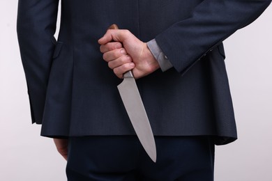 Photo of Businessman holding knife behind his back on white background, closeup