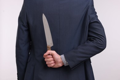 Photo of Businessman holding knife behind his back on white background, closeup