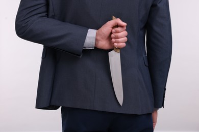 Photo of Businessman holding knife behind his back on white background, closeup