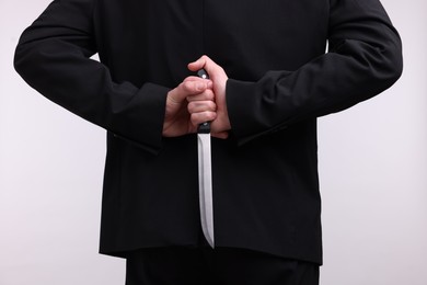 Photo of Businessman holding knife behind his back on white background, closeup