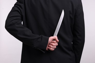 Photo of Businessman holding knife behind his back on white background, closeup