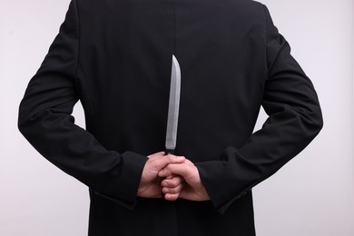 Photo of Businessman holding knife behind his back on white background, closeup